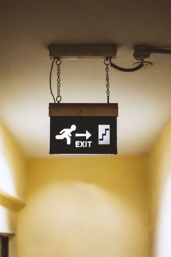 A bright exit sign hanging indoors with arrow and man running symbol pointing to stairs.